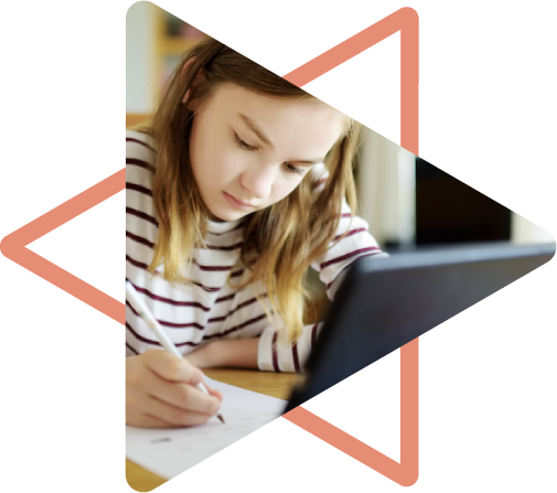 young girl sitting at laptop and writing on paper