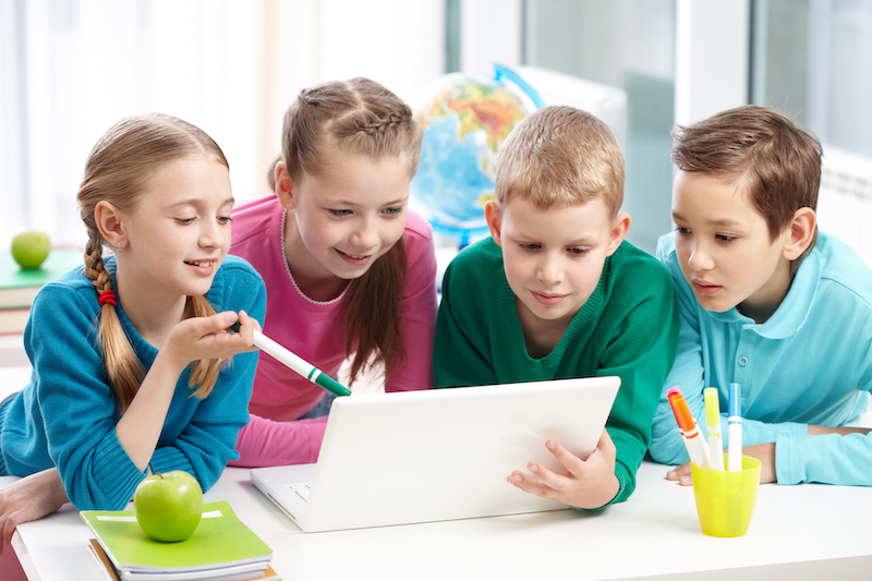 Portrait of smart schoolgirls and schoolboys looking at the laptop in classroom